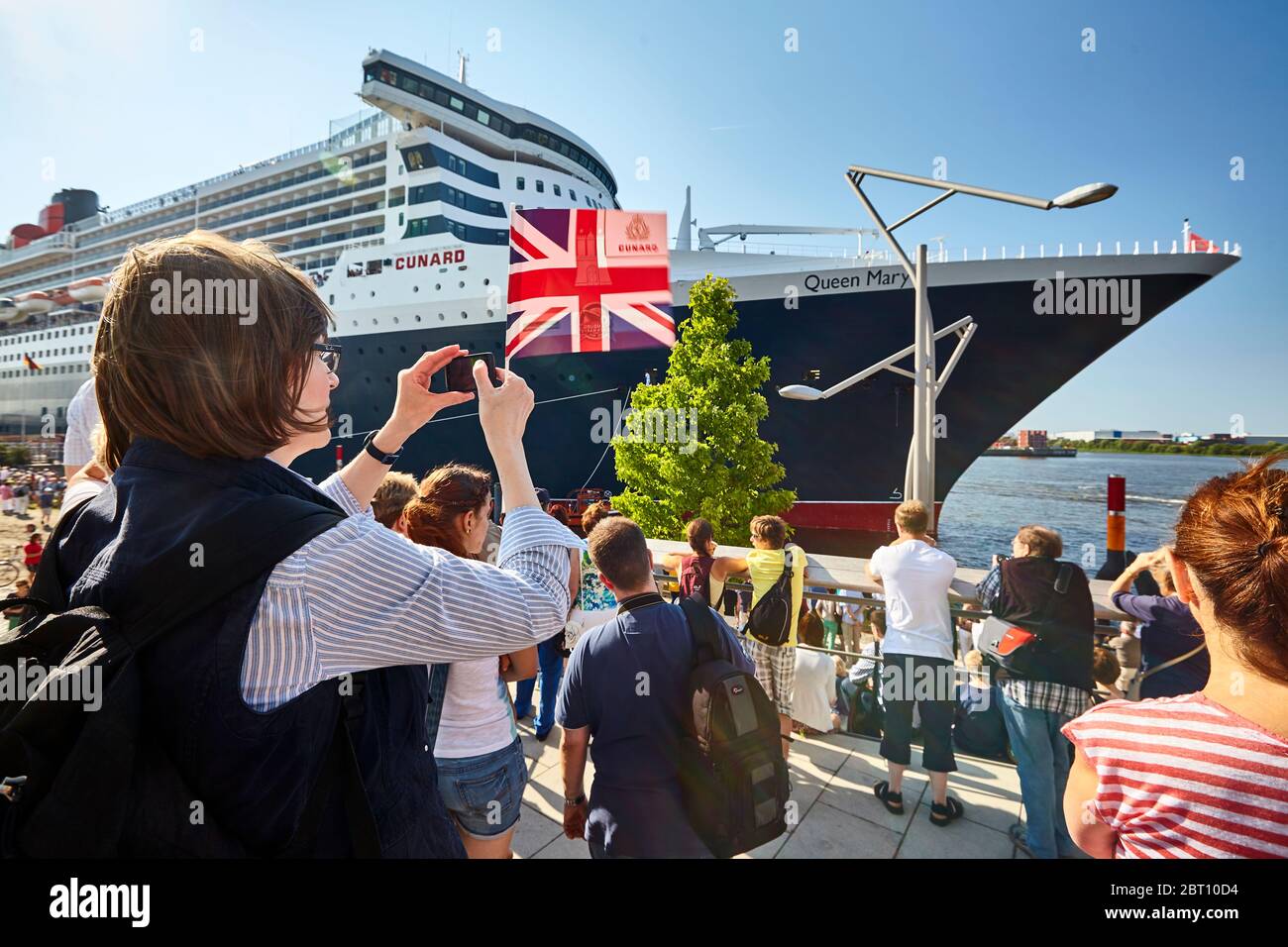 Une femme qui agite le Jack de l'Union britannique et prend des photos de la reine Marie RMS 2 au terminal de la crieuse dans le port de Hambourg. Banque D'Images