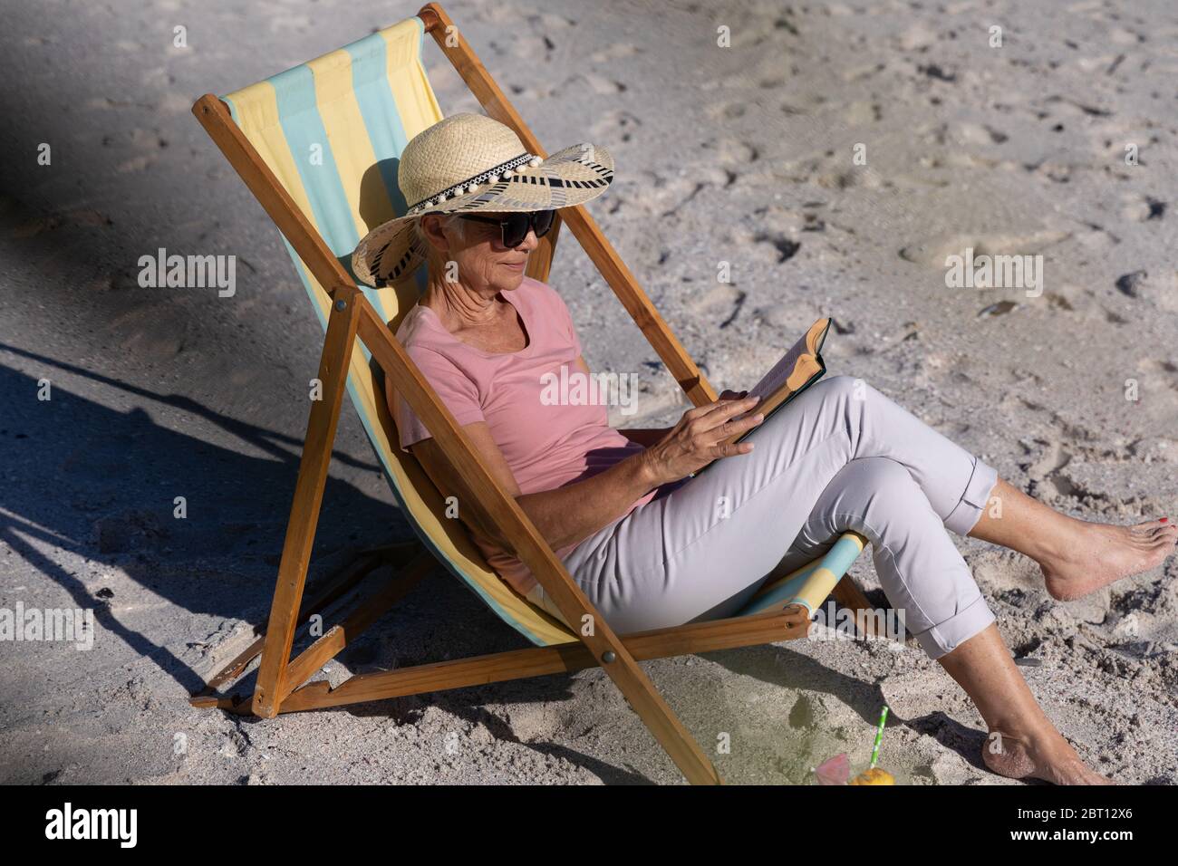 Femme de race blanche assise sur une chaise longue et lisant à la plage. Banque D'Images