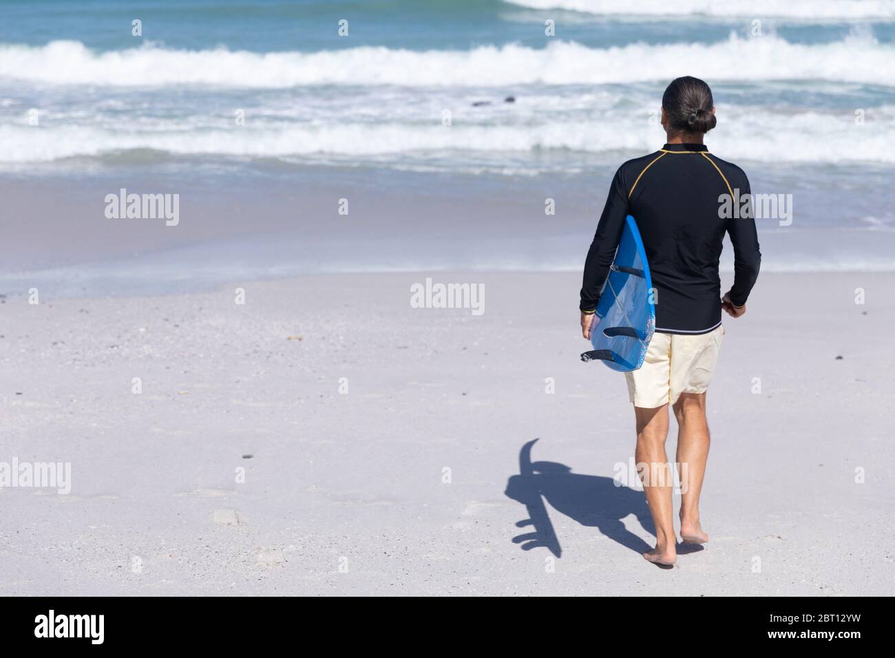 Homme caucasien senior tenant une planche de surf à la plage. Banque D'Images