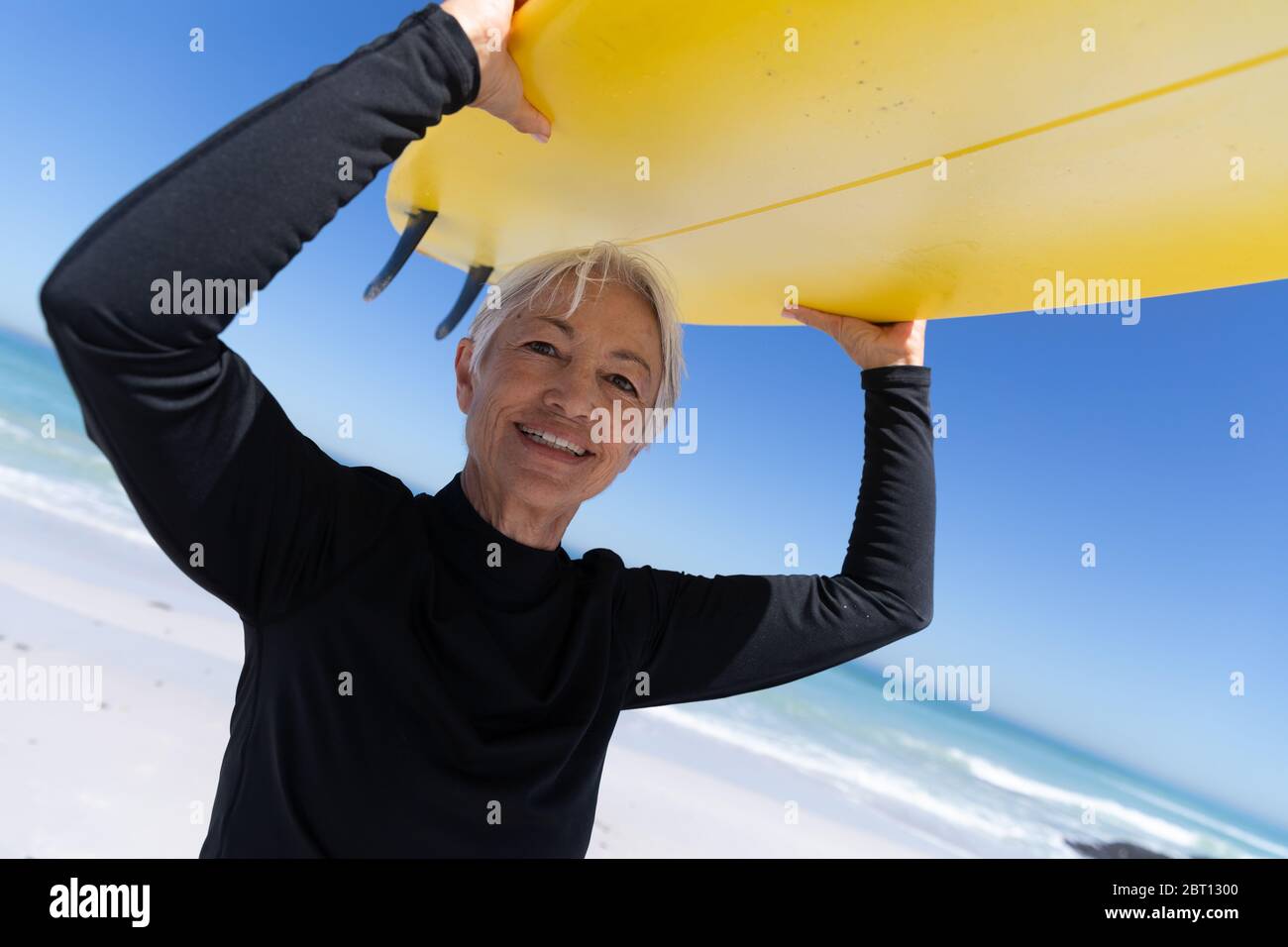 Femme caucasienne senior tenant une planche de surf à la plage. Banque D'Images