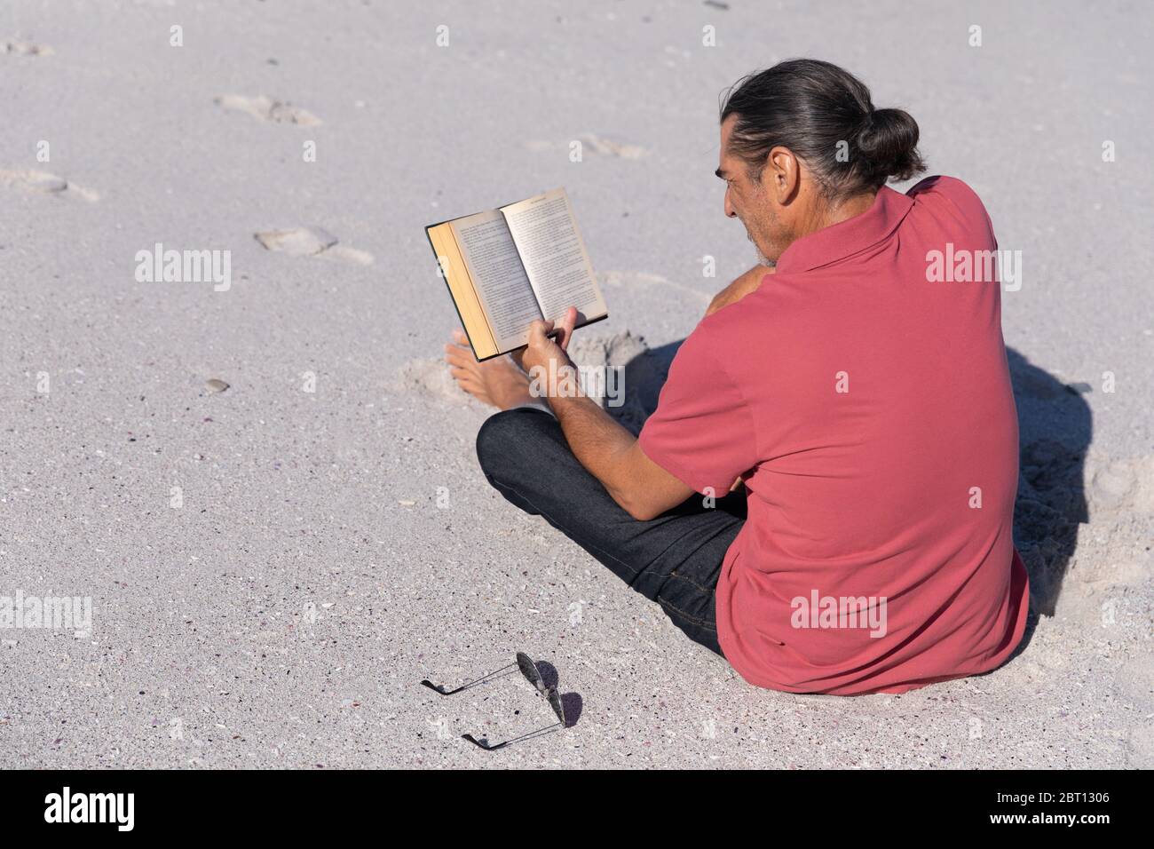 Homme caucasien senior lisant un livre à la plage. Banque D'Images
