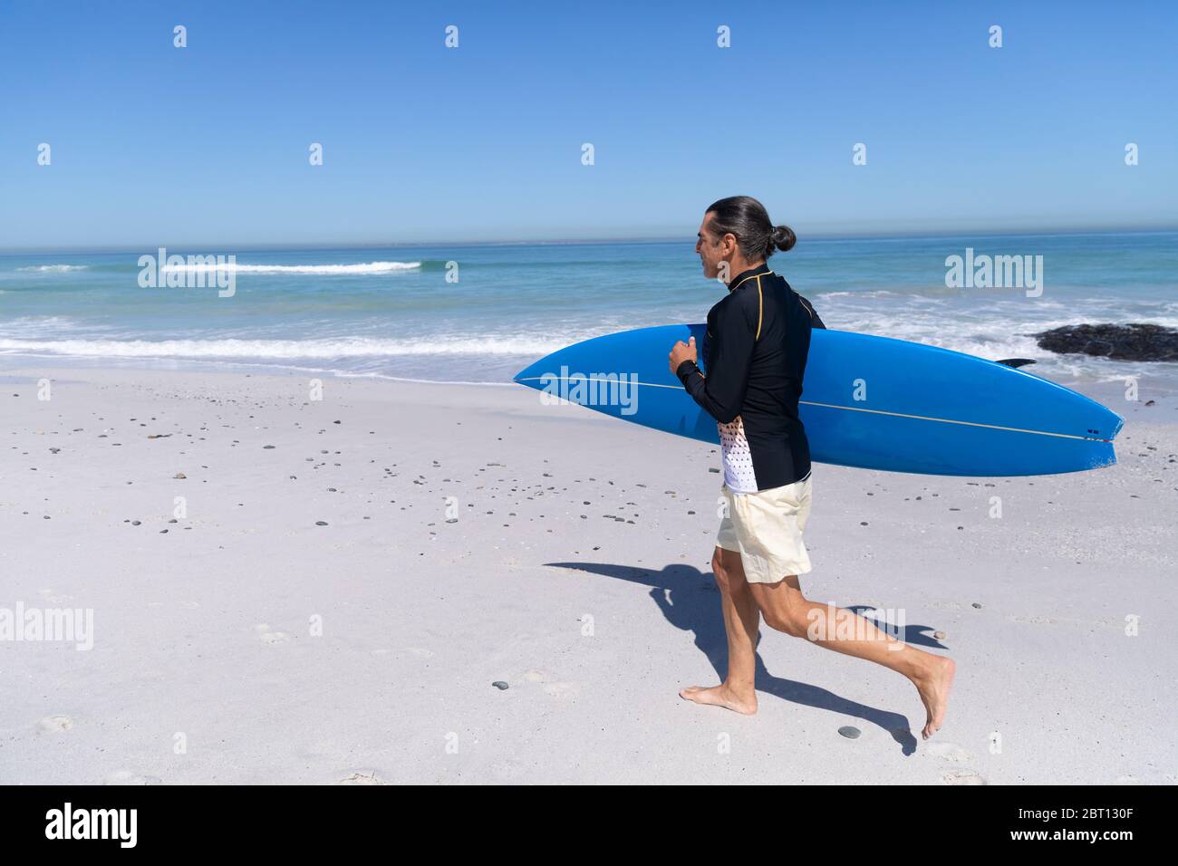 Homme caucasien senior tenant une planche de surf à la plage. Banque D'Images