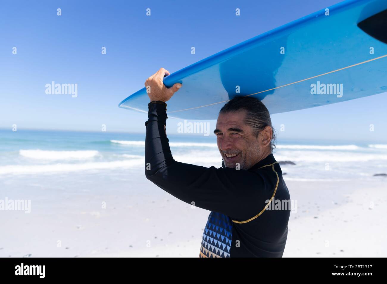 Homme caucasien senior tenant une planche de surf à la plage. Banque D'Images