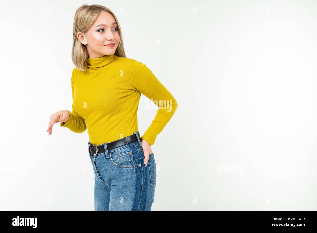 blonde fille dans une veste et un jean jaune ajusté posant sur le côté sur un fond blanc. Banque D'Images