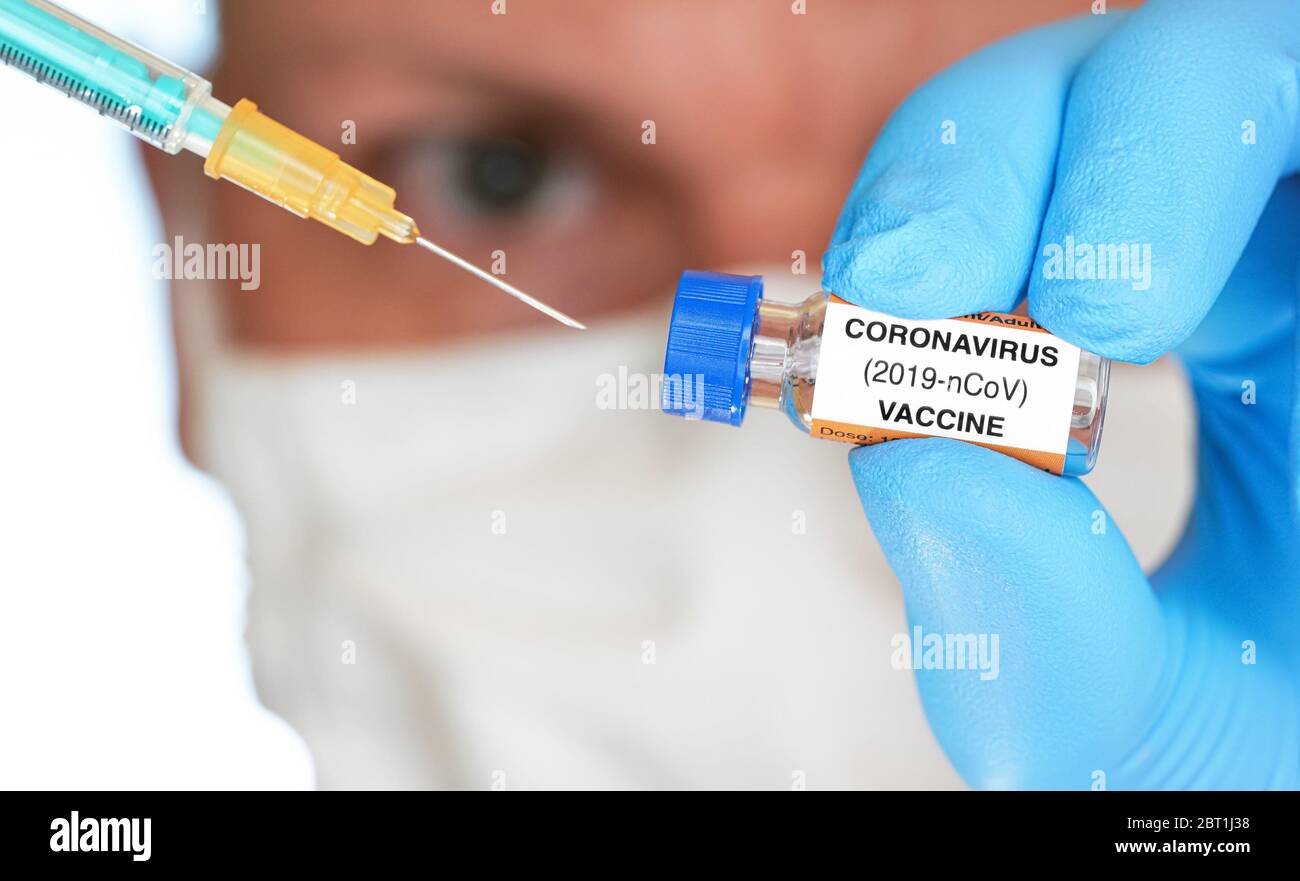 Main d'homme dans un gant bleu en nitrile tenir un petit flacon avec le vaccin coronavirus, pour l'injecter avec une seringue orange verte, visage flou avec masque blanc de virus dedans Banque D'Images