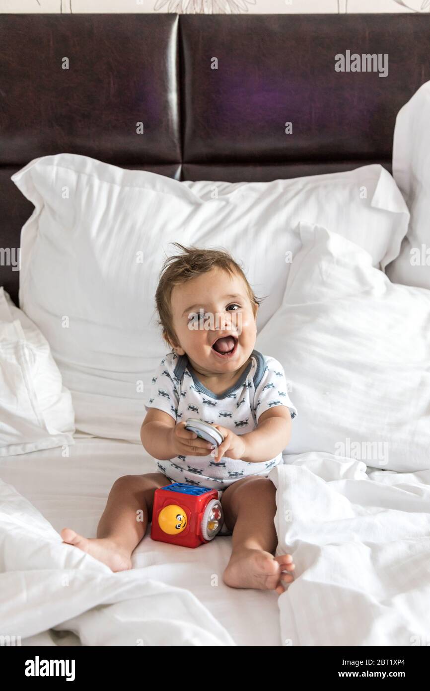Bébé garçon heureux assis sur un lit jouant avec un jouet Banque D'Images