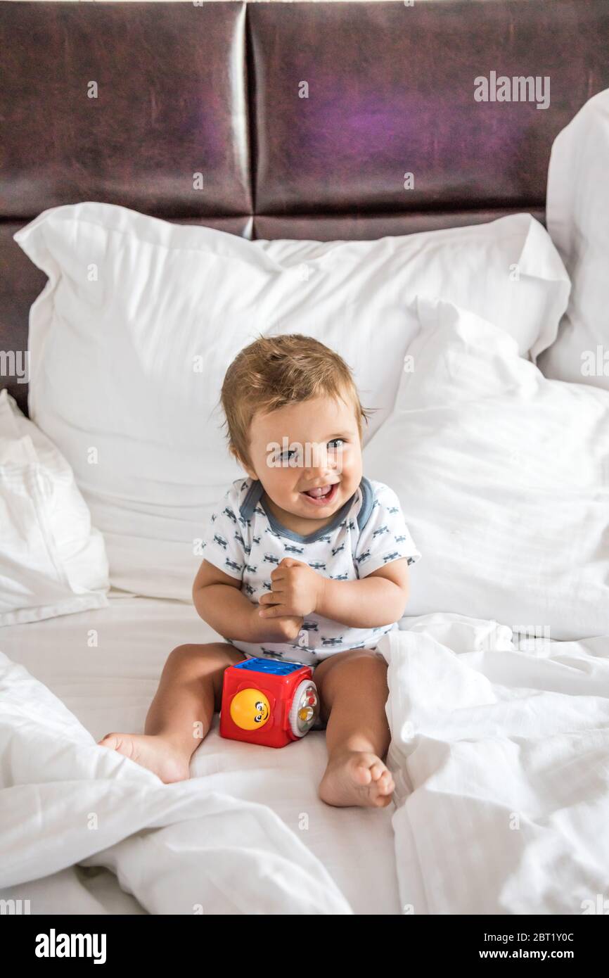 Bébé garçon heureux assis sur un lit jouant avec un jouet Banque D'Images