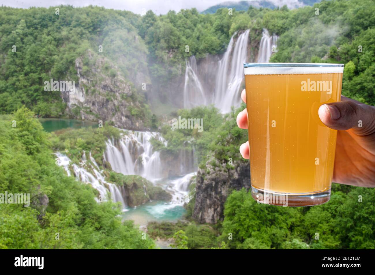 Homme tenant un verre de bière légère sur fond de grande cascade. Détendez-vous, reposez-vous dans la nature. Banque D'Images