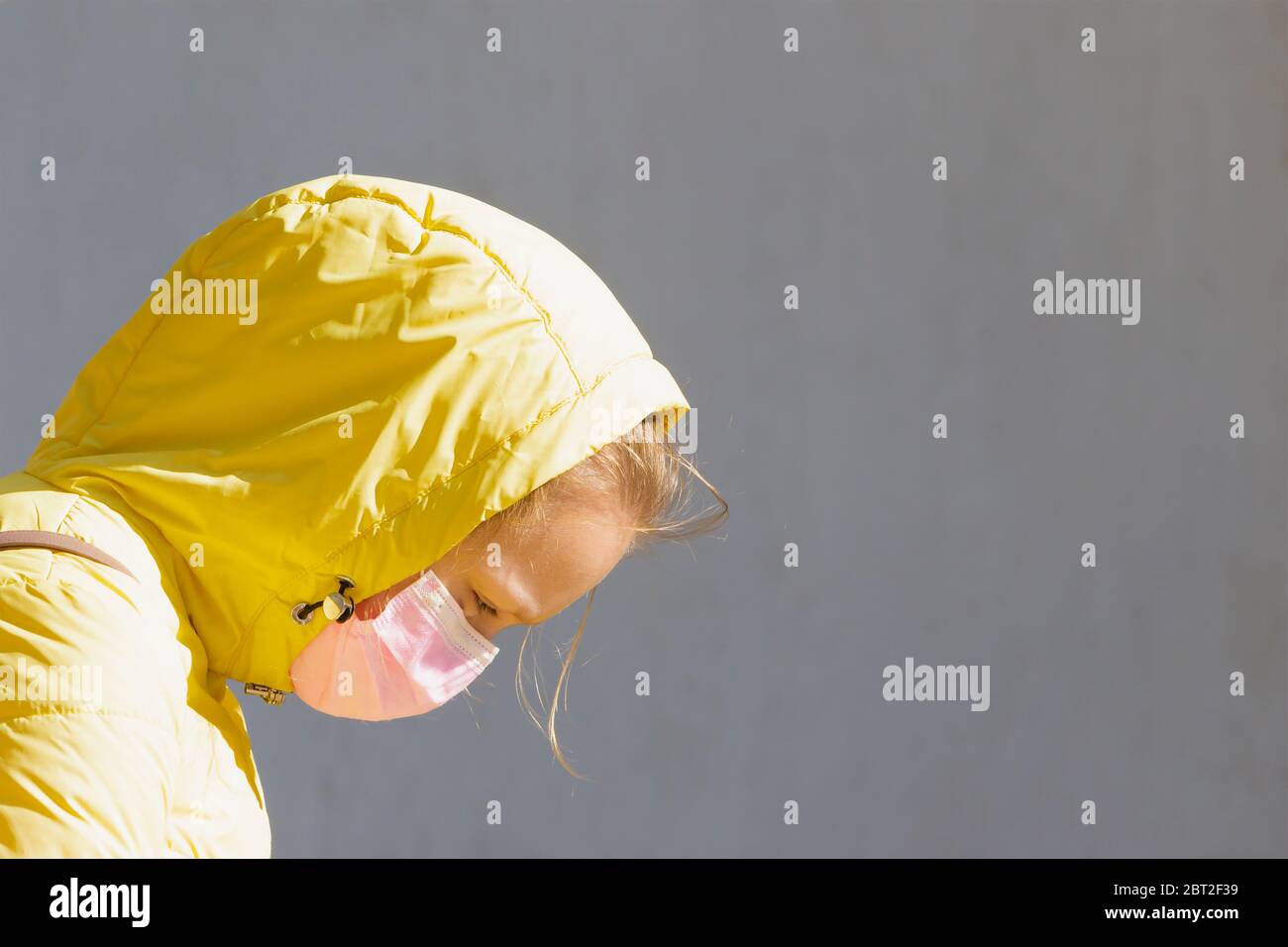 Fille dans un masque médical et une cagoule jaune sur fond gris avec espace libre. Banque D'Images