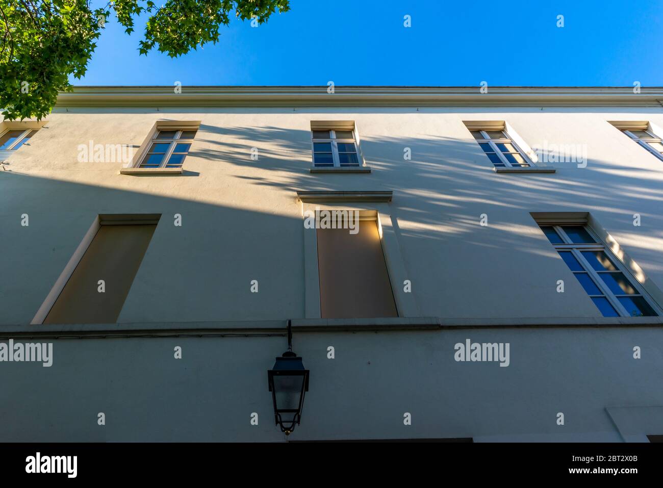 Vue à angle bas d'une façade beige pâle avec lanterne extérieure et ombres à moulages de feuillage, Butte-aux-Cailles, Paris, France Banque D'Images