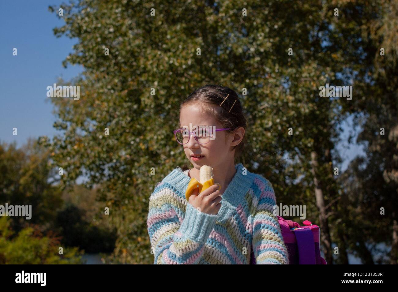 Écolière mangeant une banane dans la rue. Les enfants de la génération alpha seront la force motrice du progrès dans notre siècle. Ils sont plus équilibrés, Banque D'Images