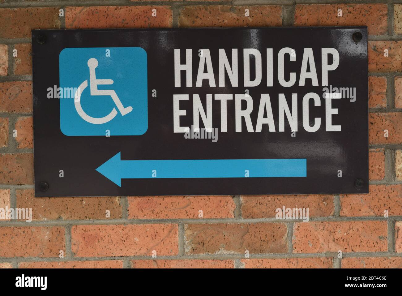 Une entrée pour handicapés signe un mur de briques dans un parking avec une flèche et un pictogramme de fauteuil roulant dirige les clients handicapés vers un A. Banque D'Images