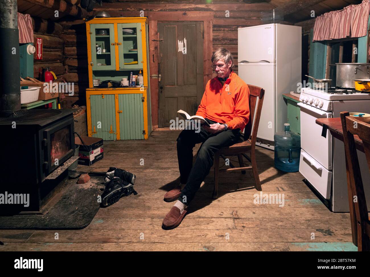 MT00506-00....MONTANA - Tom qui apprécie une lecture en soirée au coin du poêle à bois dans une cabine de location dans la ville fantôme de Garnet. Banque D'Images