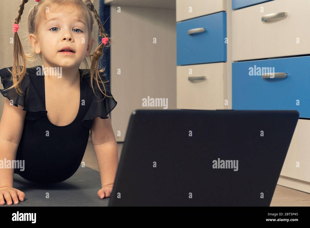 une petite fille dans un léopard de gymnastique noir fait de la gymnastique à la maison en ligne devant un ordinateur portable. gymnastique rythmique à distance pour les enfants Banque D'Images