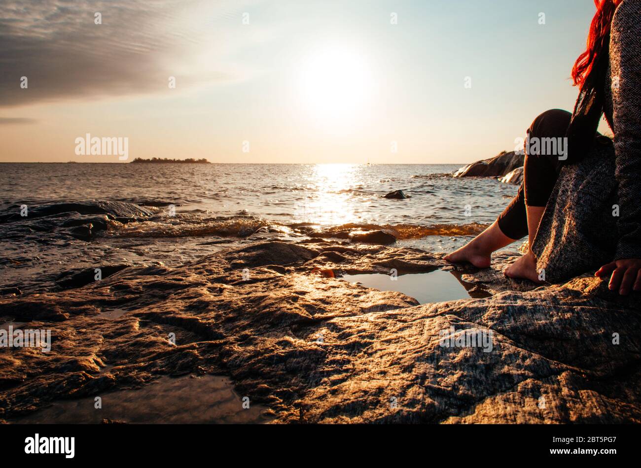 Une capture à couper le souffle de l'heure d'or à Colonia Del Sacramento, en Uruguay avec une vue sur le Rio de la Plata avec une fille assise dans les rochers. Banque D'Images