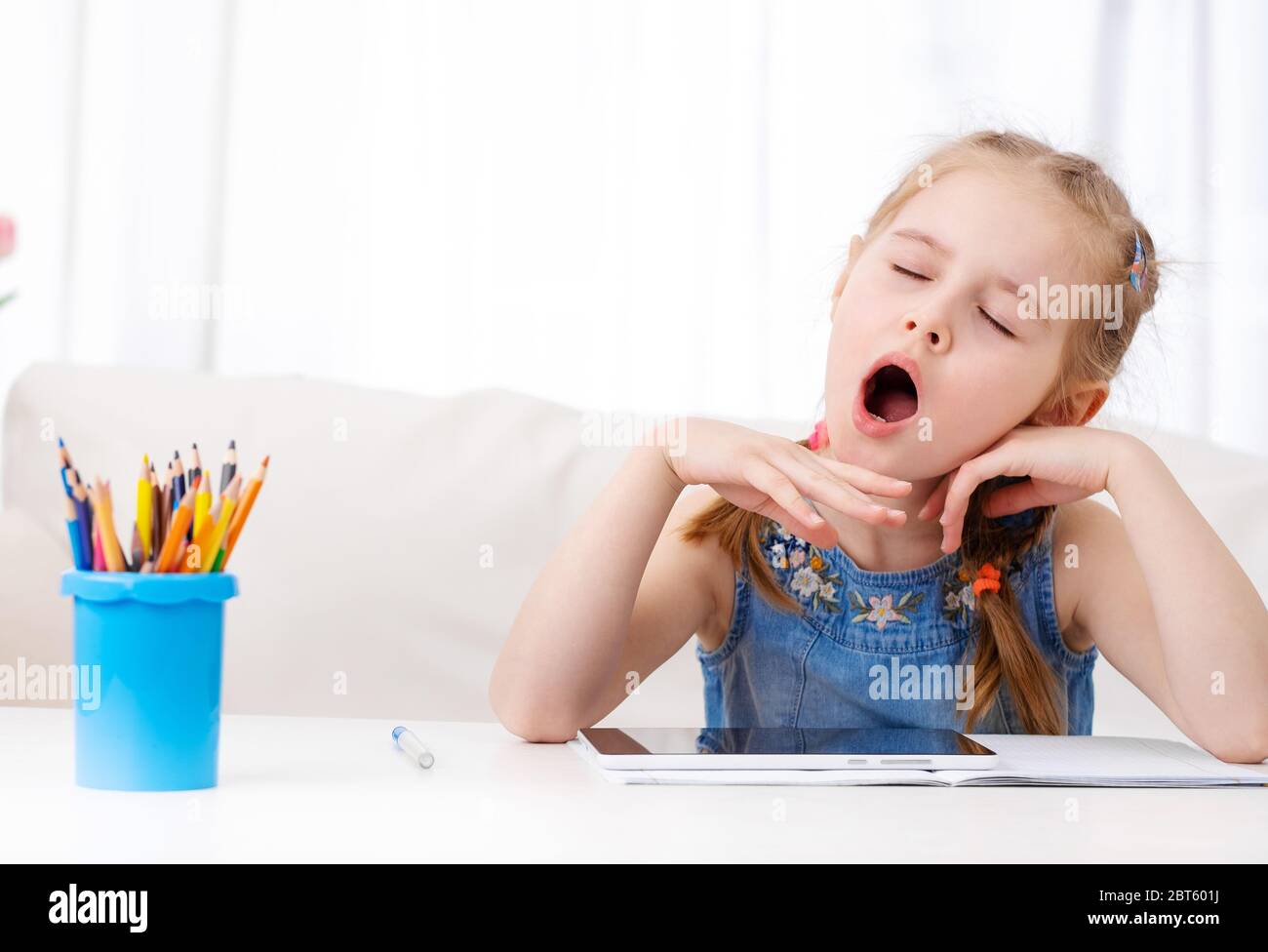 Une petite fille qui bâille lors de ses devoirs avec une tablette numérique Banque D'Images