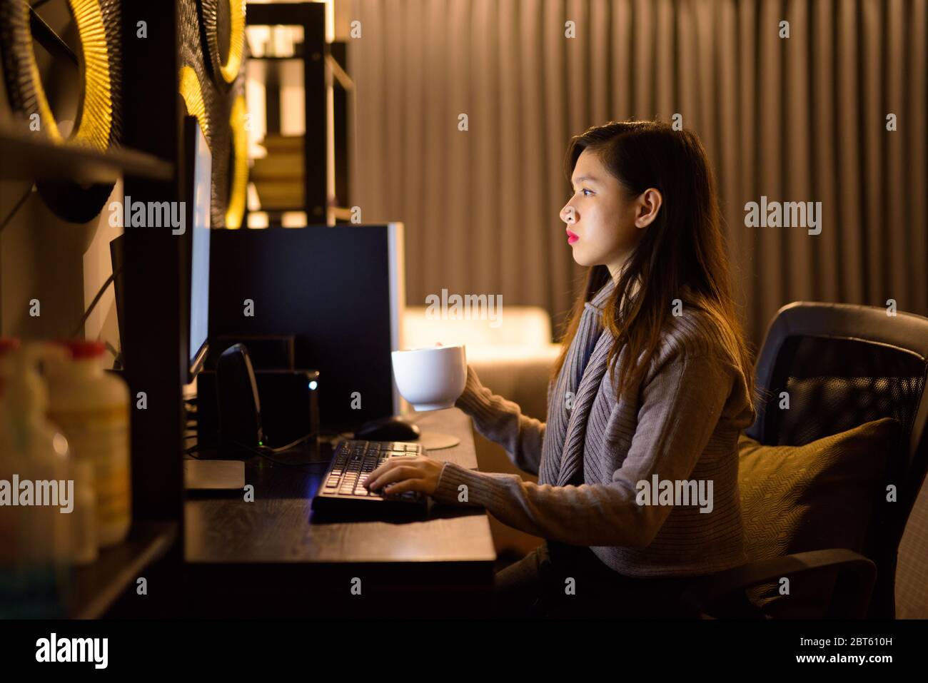 Jeune femme asiatique qui boit du café en travaillant de chez elle tard dans la nuit Banque D'Images