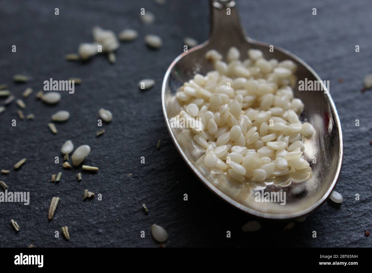 Une cuillère à café de graines de sésame blanc sur fond d'ardoise. Ingrédients crus pour la cuisson. Allergène alimentaire Banque D'Images