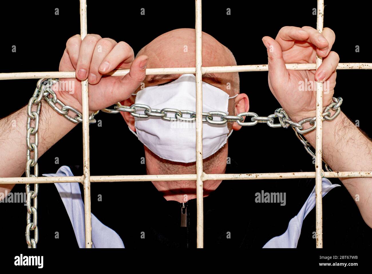 Confinement pandémique et concept de quarantaine Bald homme d'âge moyen dans un masque d'hygiène médicale derrière des barres de fer chaînées Banque D'Images