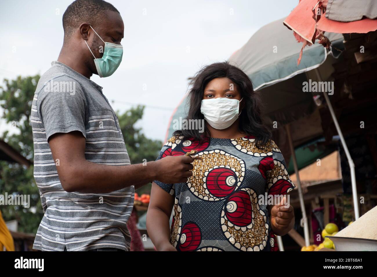 femme africaine sur un marché local portant un masque facial vendant à un client qui recueille de l'argent Banque D'Images