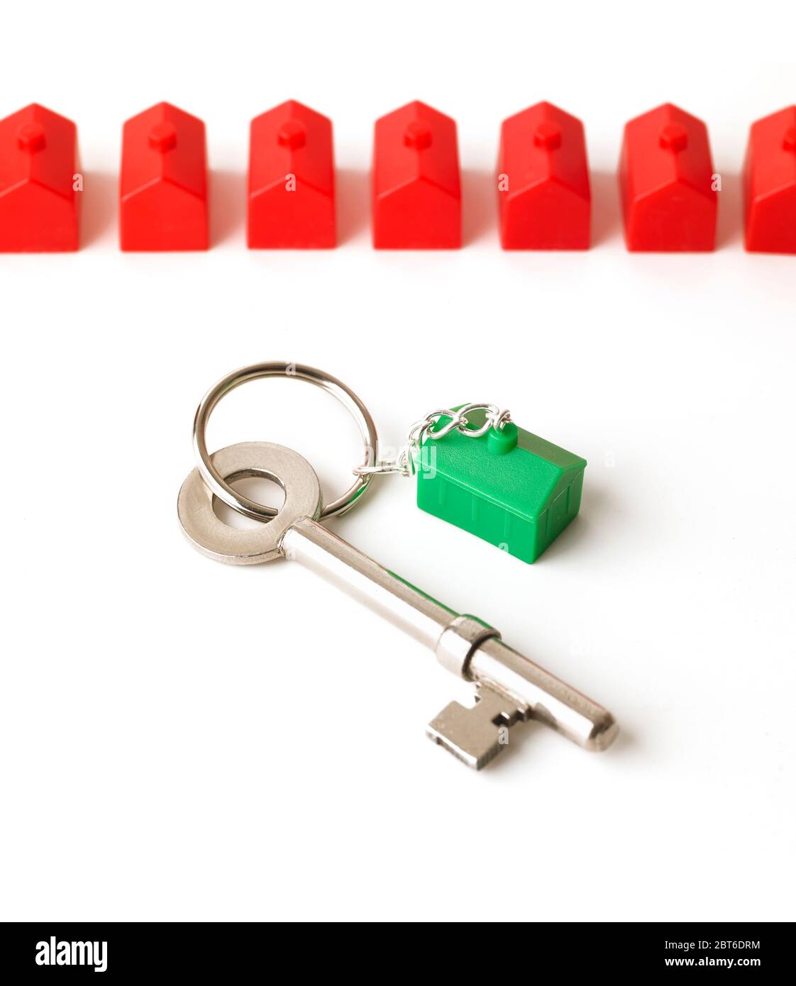 Clé de maison avec maison en plastique vert, rangée de maisons rouges similaires en arrière-plan Banque D'Images
