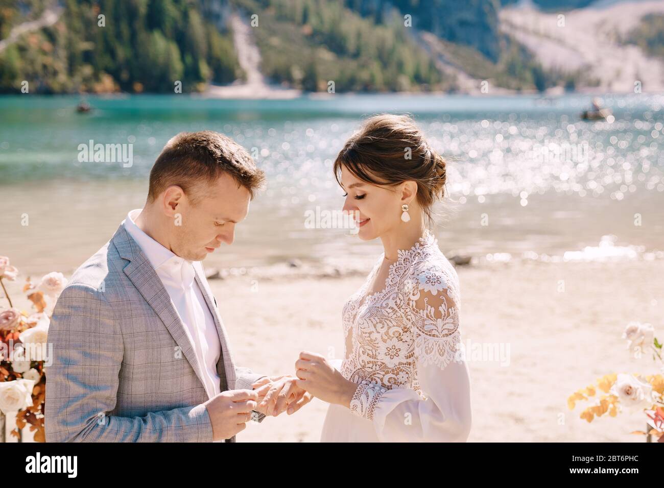 Le marié met un anneau à la mariée, au lieu de la cérémonie, avec une arche de colonnes de fleurs d'automne, sur fond de Lago di Braies dedans Banque D'Images