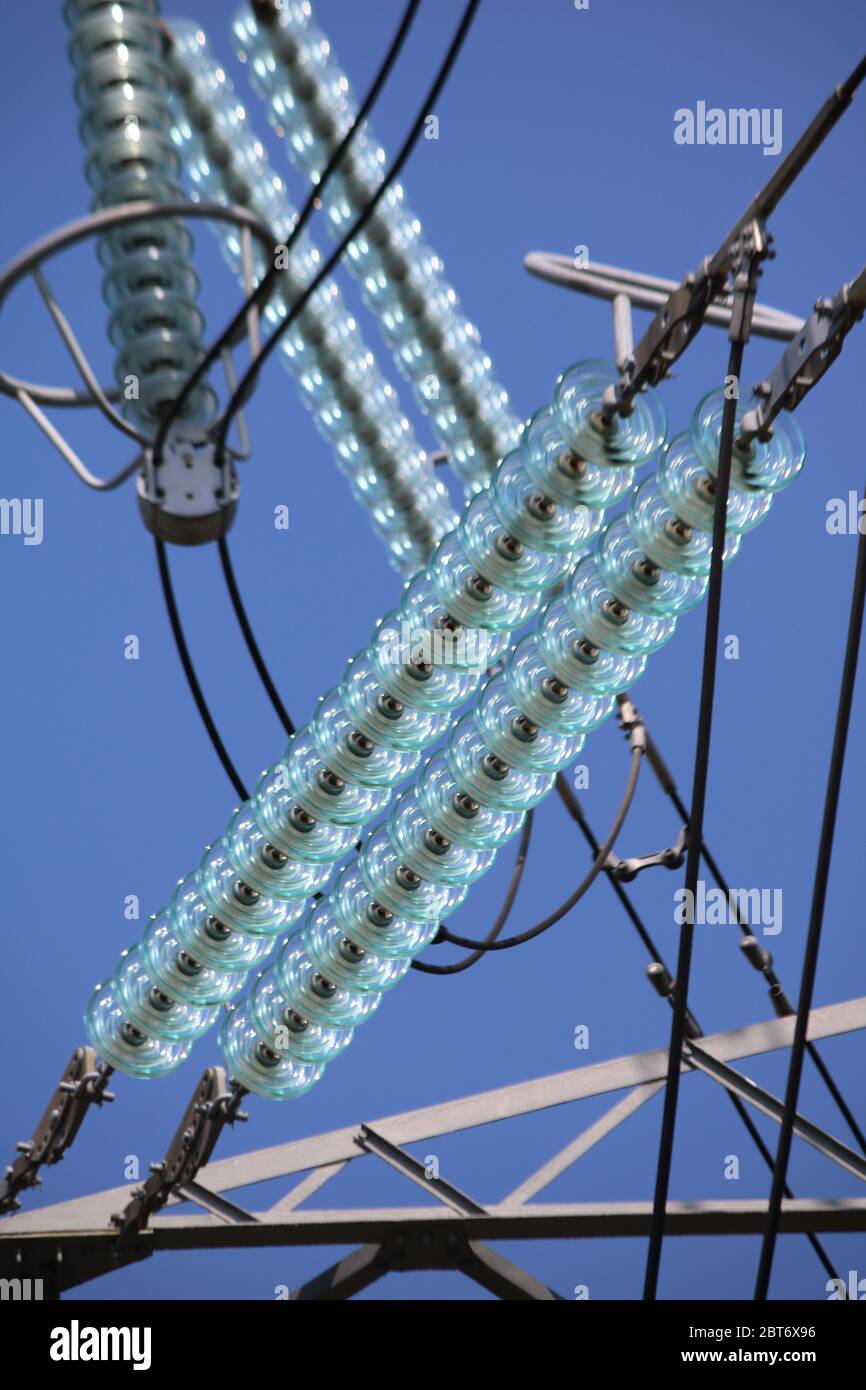 Disques isolants en verre bleu sur les fils électriques qui se croisent contre un ciel bleu clair Banque D'Images