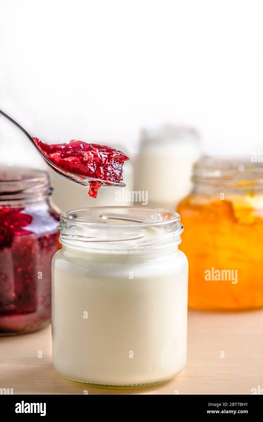 Yaourt maison avec marmelade de baies rouges cueillies dans un pot en verre sur une table en bois blanc. Petit déjeuner probiotique laitier sain avec espace pour les copies Banque D'Images