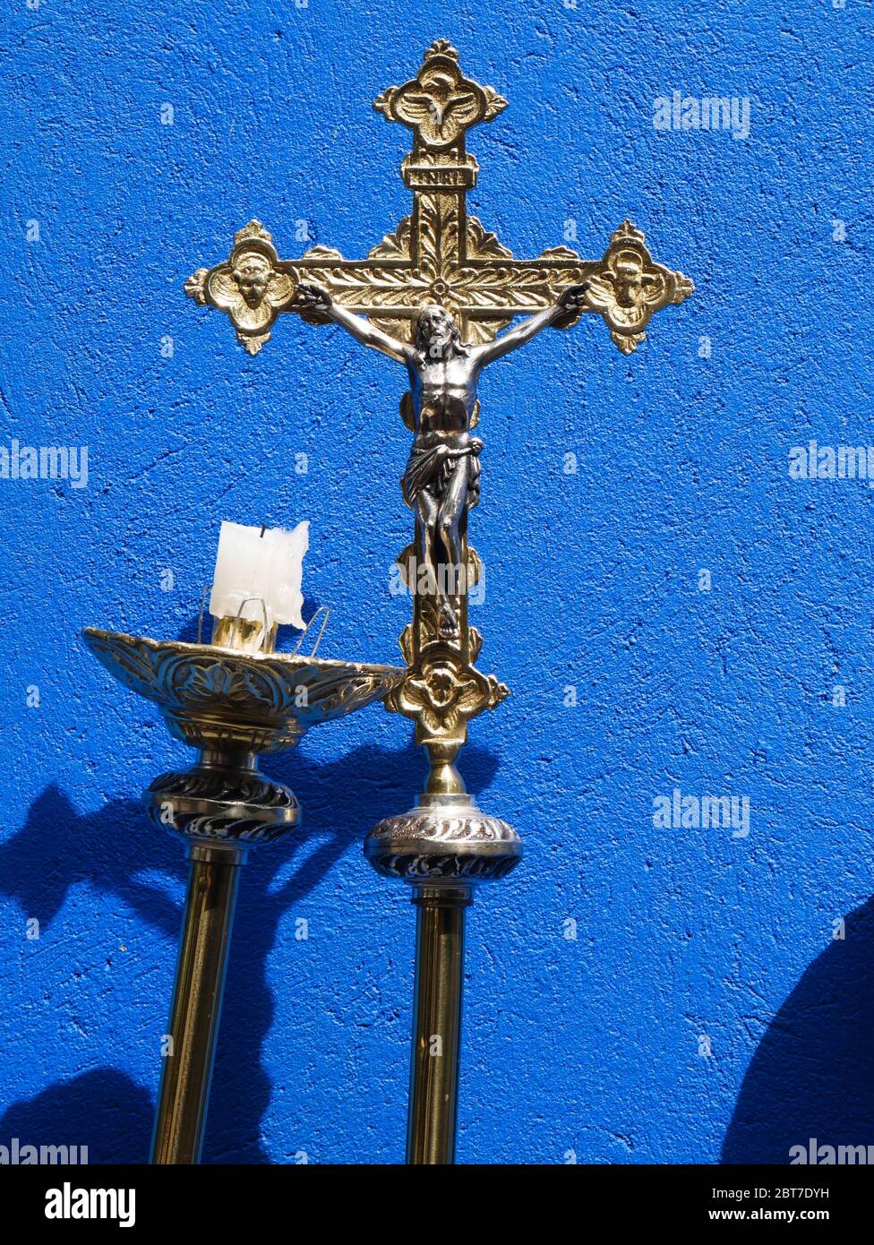 Croix métallique pour la célébration catholique avec fond bleu et lustre avec bougie à moitié brûlée verticale Banque D'Images