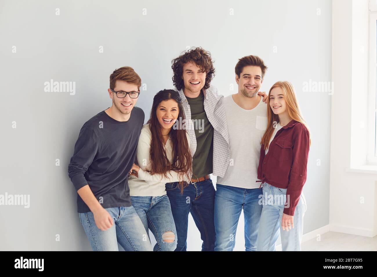 Groupe de jeunes étudiants dans des vêtements décontractés souriant tout en se tenant sur fond gris. Amis ensemble sur un mur gris. Étudiants d'amitié. Banque D'Images