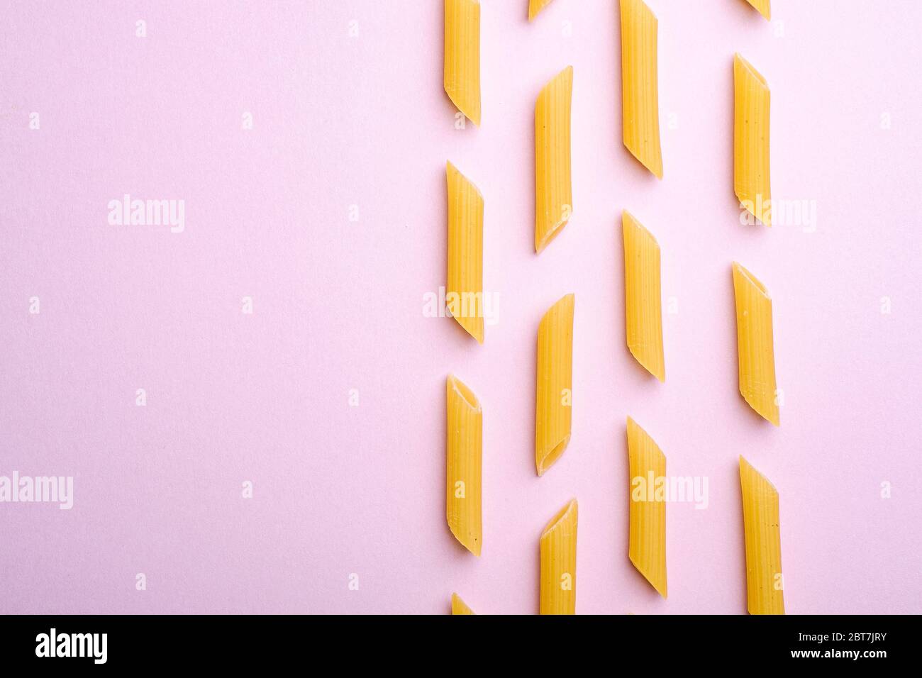 Pâtes italiennes, motif macaroni en tube de penne brut sur fond rose, espace de copie avec vue de dessus, nourriture abstraite Banque D'Images