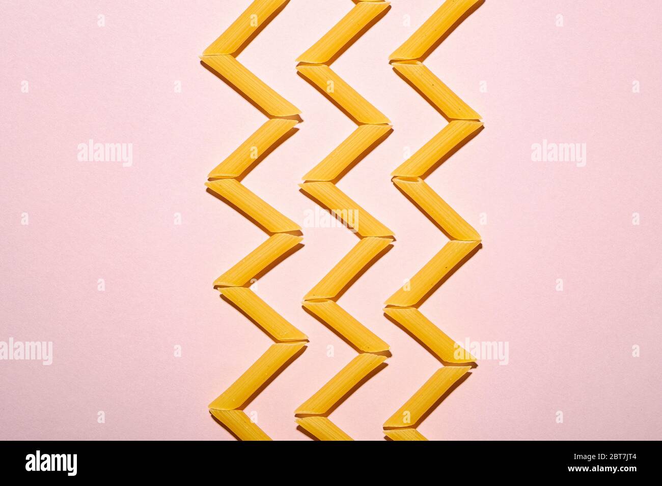 Pâtes italiennes, tube de penne cru macaroni en zigzag sur fond rose, espace de copie avec vue du dessus, nourriture abstraite Banque D'Images