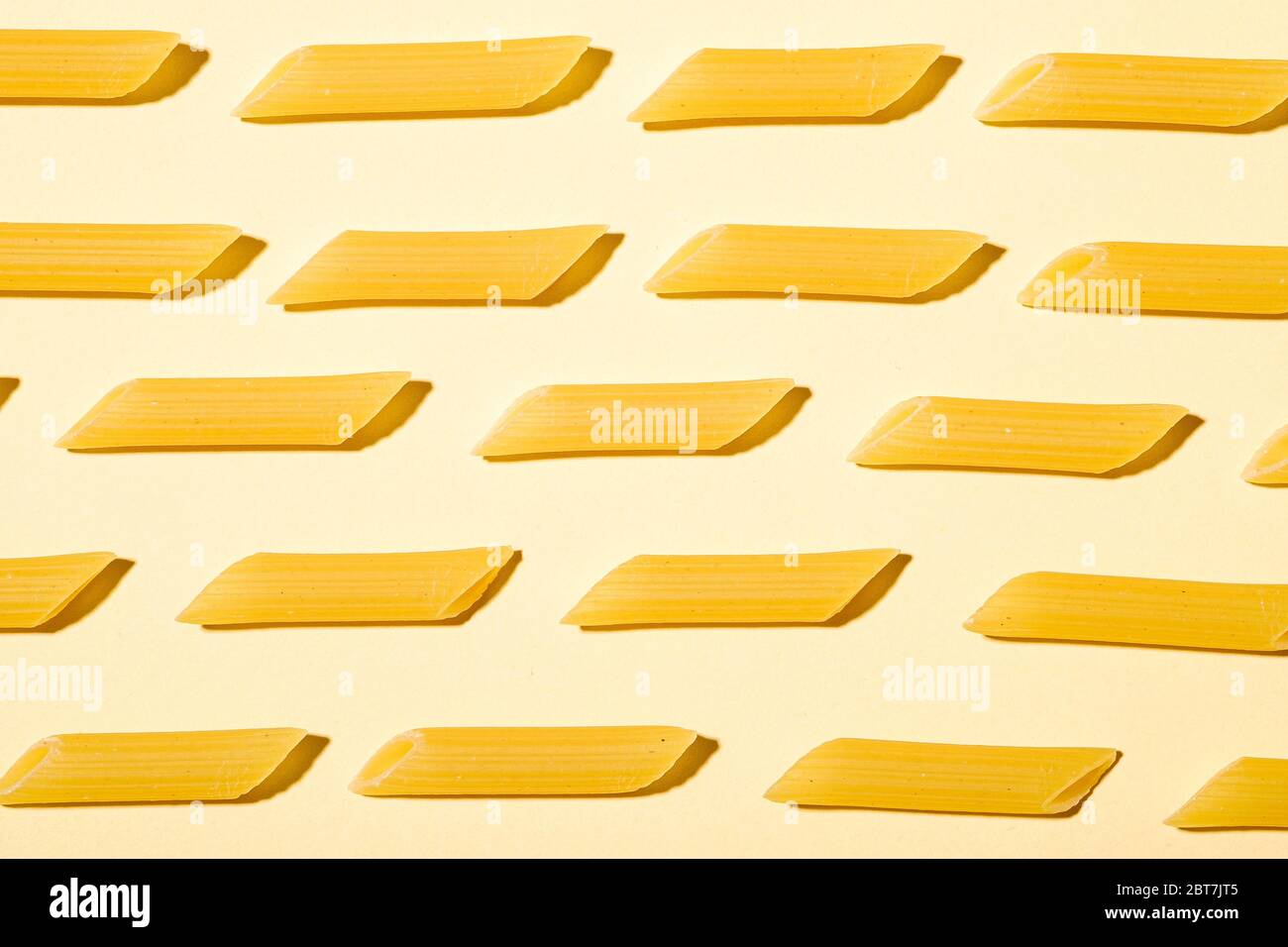 Pâtes italiennes, motif macaroni en tube de penne brut sur fond jaune crème, vue du dessus, nourriture abstraite Banque D'Images