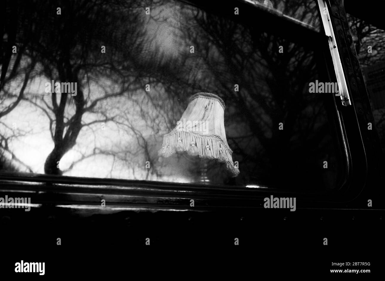 Lampe à l'ancienne à la fenêtre du bus fantôme garée à Édimbourg pendant le confinement 2020 avec des reflets d'arbres dans les fenêtres. Noir et blanc spectaculaire. Banque D'Images