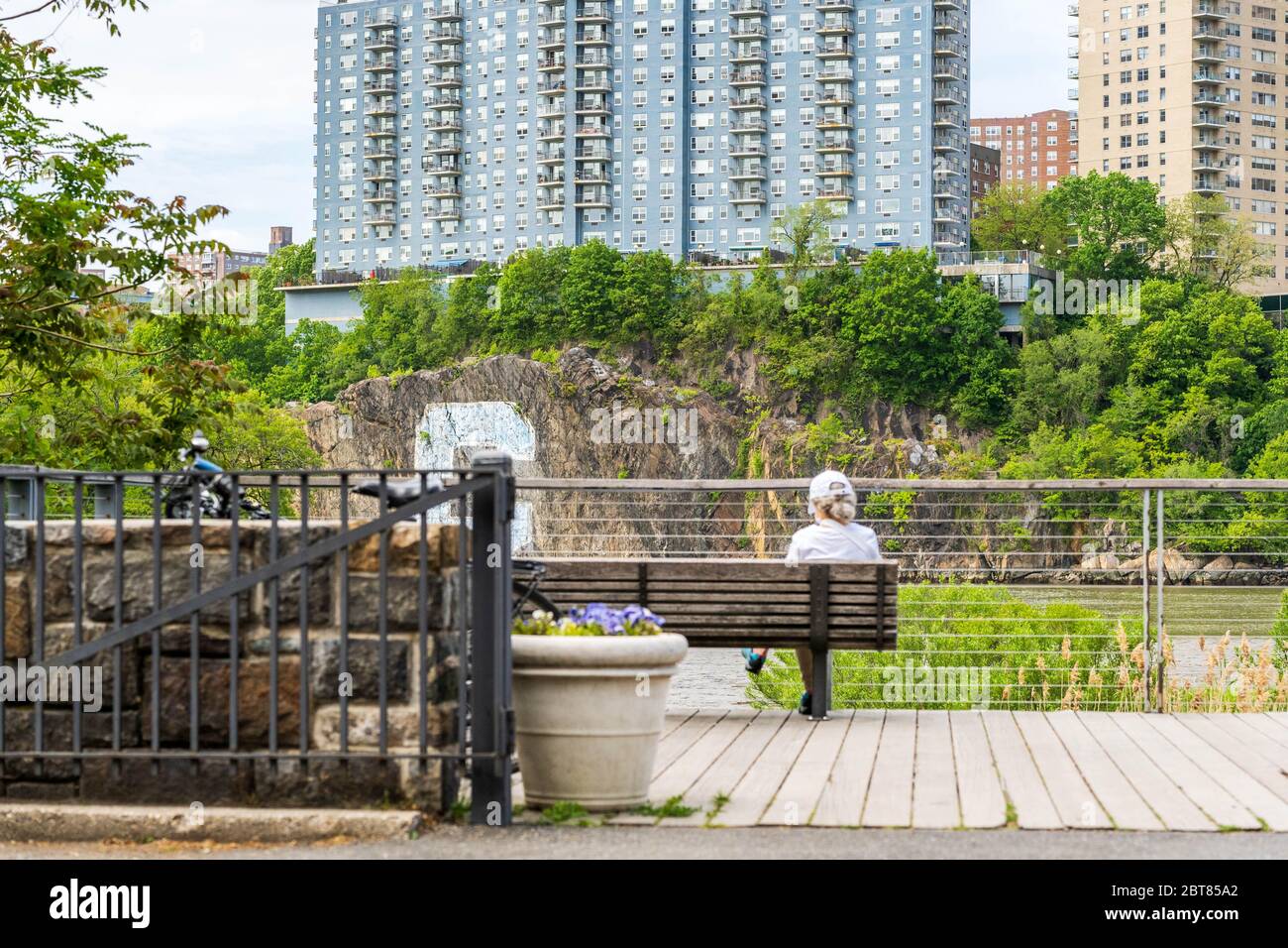 Une femme âgée est assise sur UN banc de parc et bénéficie de la vue sur le parc Inwood Hill. Banque D'Images