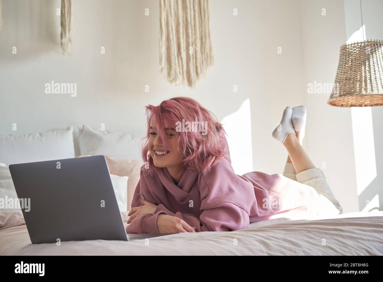 Bonne hipster gen z teen fille avec les cheveux roses regarder le film sur ordinateur portable dans le lit. Banque D'Images