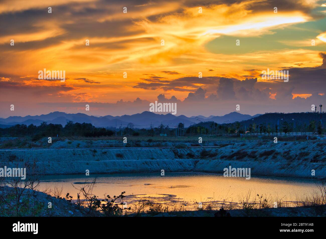 Cette photo unique montre un ciel rouge vif de coucher de soleil reflété dans un lac. En arrière-plan, vous pouvez encore voir les montagnes de Hua Hin en Thaïlande très bien Banque D'Images
