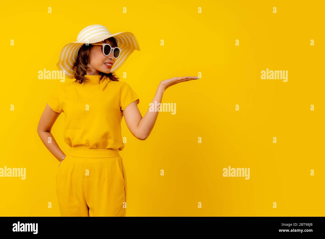 Mignon et drôle gai femme debout dans jaune décontracté style de tissu montrer main vide pour le produit en vente à des achats Banque D'Images