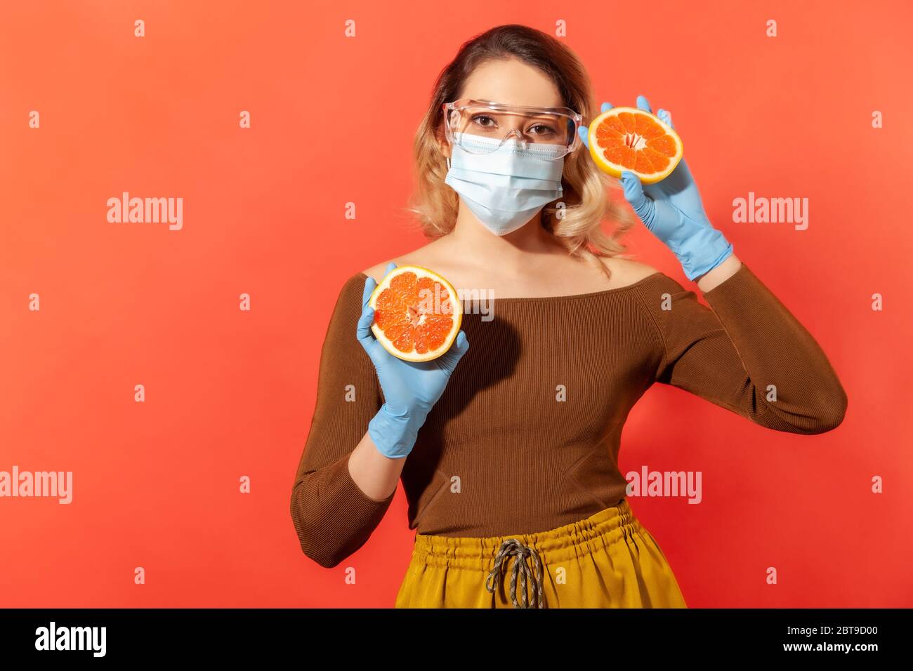 Femme en lunettes de protection, masque, gants tenant des fruits frais orange, vitamines naturelles pour le système immunitaire et le traitement de la grippe, une nutrition saine pendant q Banque D'Images