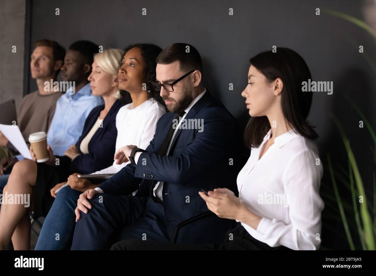 Divers candidats en attente d'un entretien d'embauche, assis en rangée Banque D'Images