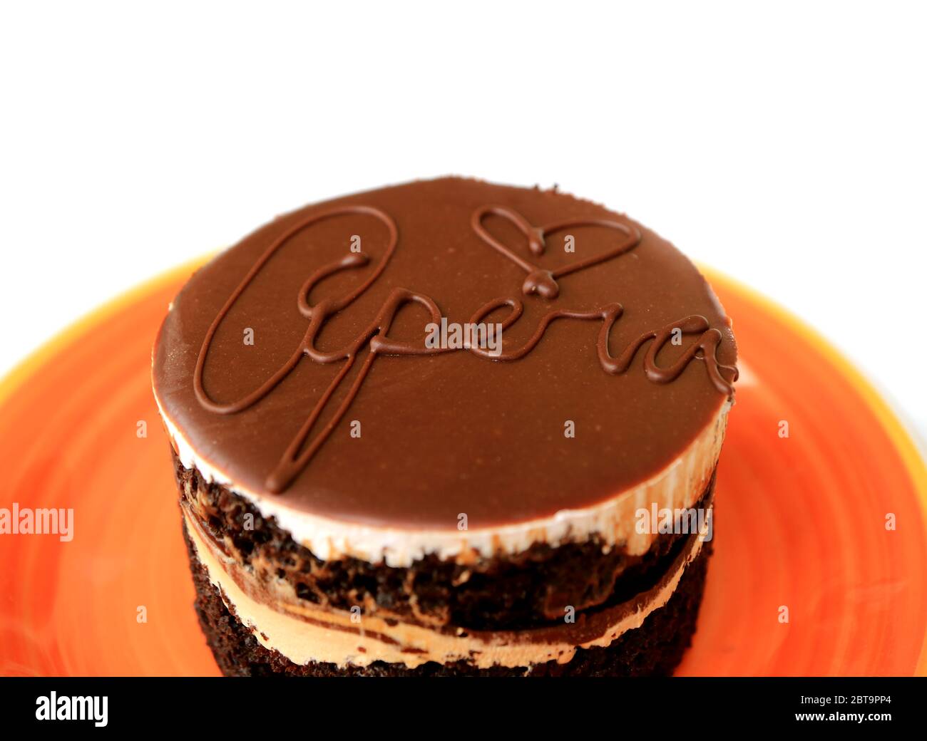 Gros plan un savoureux gâteau d'opéra rond servi sur une assiette d'orange vif isolée sur fond blanc Banque D'Images