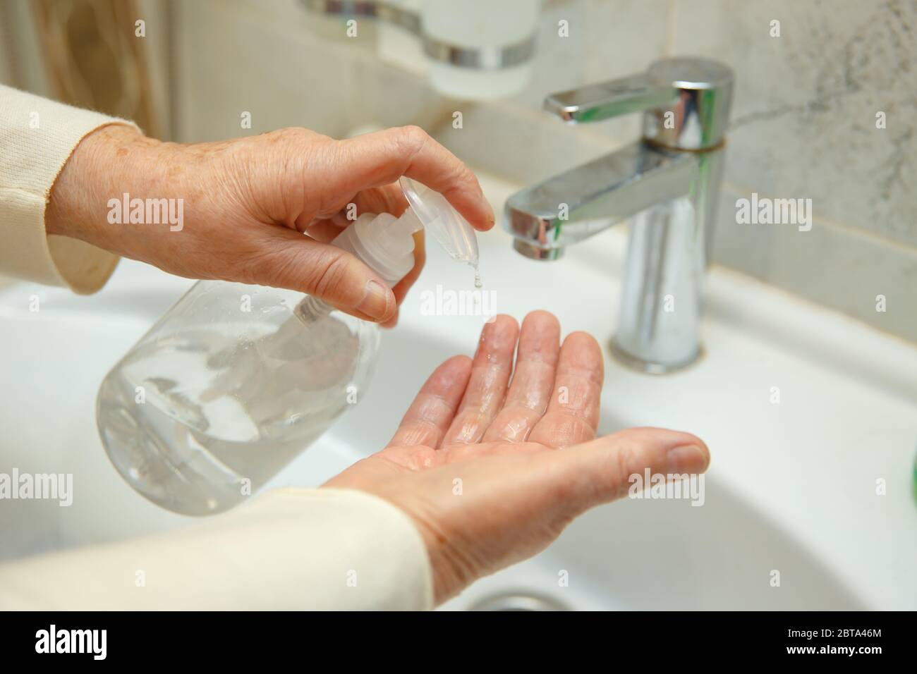 Une femme âgée désinfecte ses mains dans la salle de bains. Banque D'Images