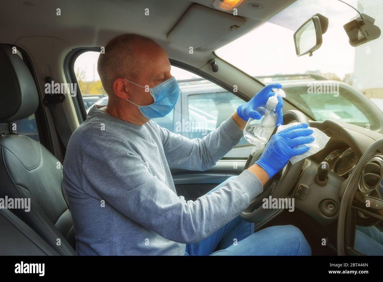 Désinfection automobile. Un homme en gants et un masque essuie le volant avec un chiffon désinfectant. Banque D'Images