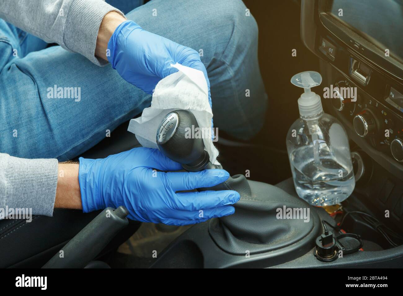 Désinfection automobile. Un homme en gants et un masque essuie le levier de vitesses avec un désinfectant. Banque D'Images