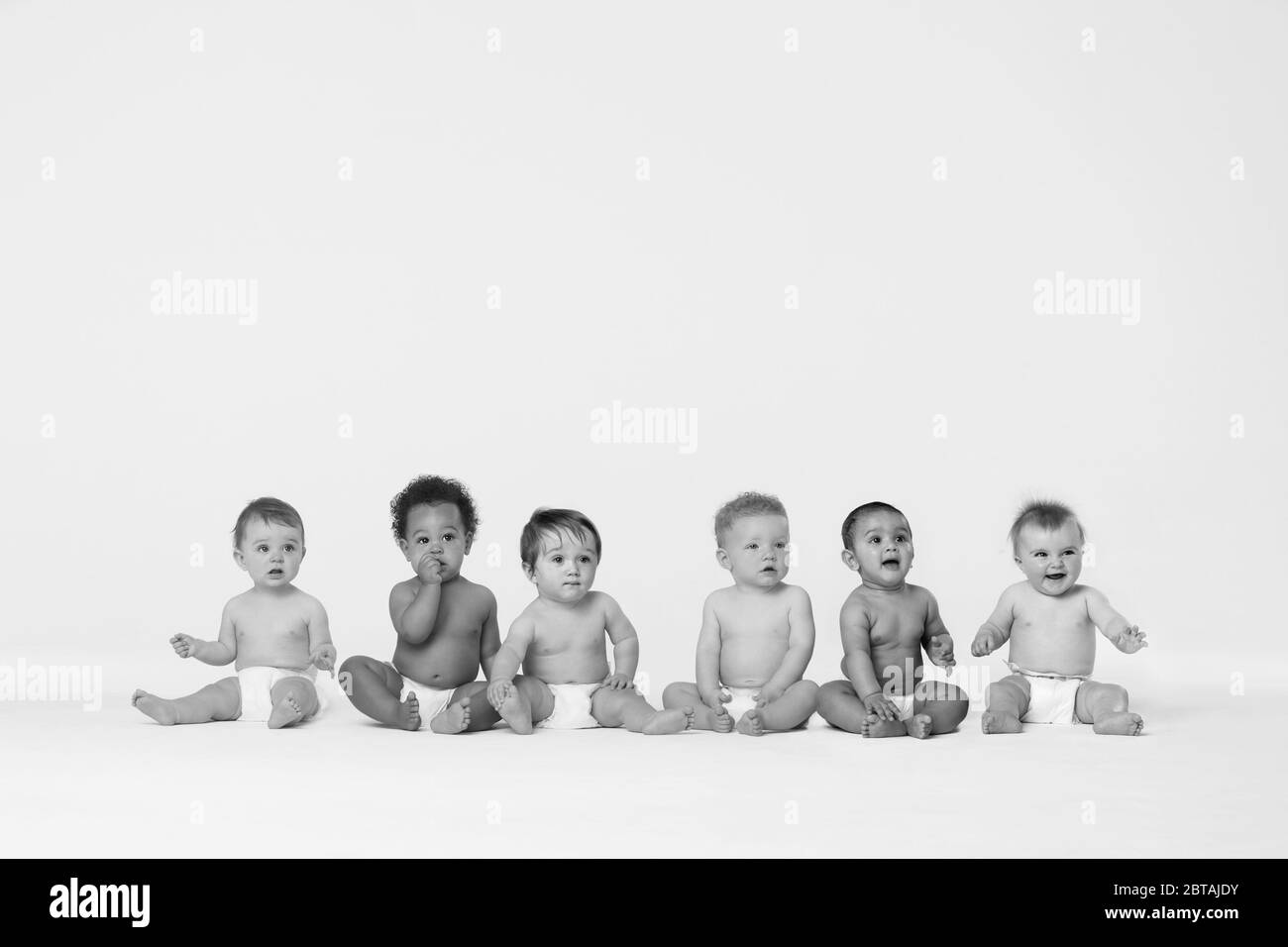 Photo en noir et blanc de la rangée de six bébés multiethniques souriant en studio Banque D'Images