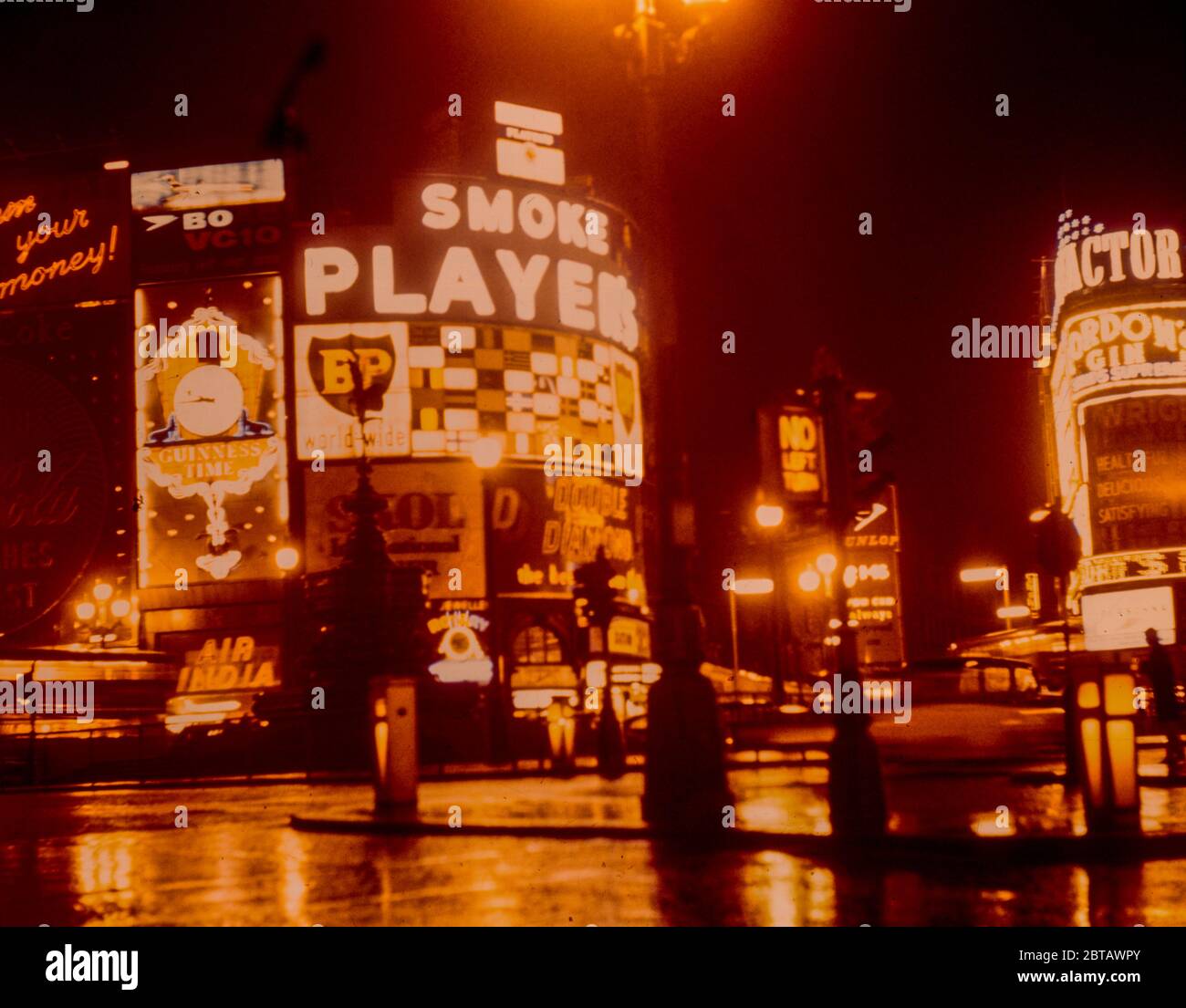 Les enseignes au néon de Piccadilly Circus se reflètent dans la pluie de nuit dans la rue, faisant la publicité des produits et des films populaires des années 1960, pris en 1961. Banque D'Images