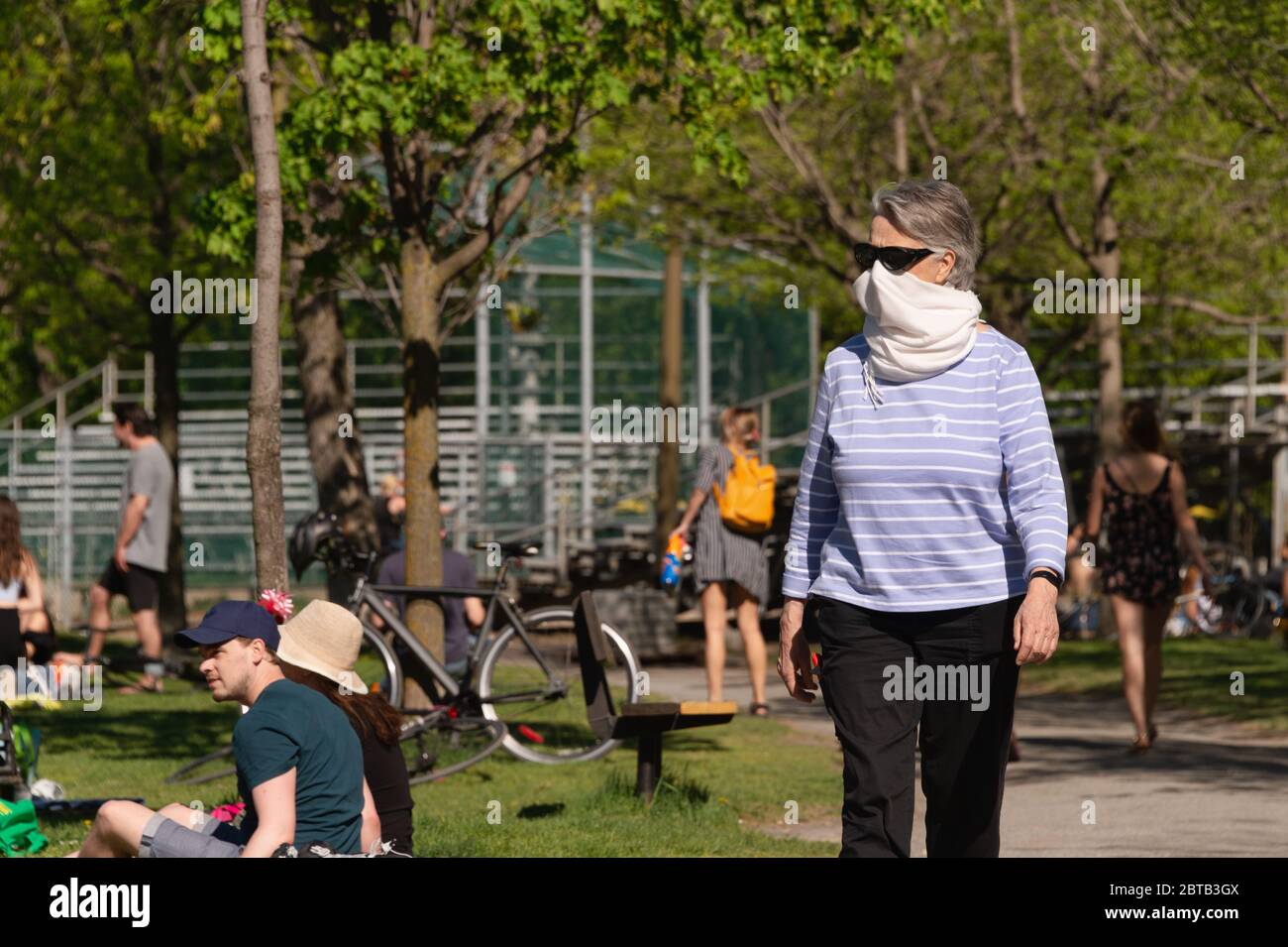 Montréal, CA - 23 mai 2020 : Femme avec écharpe pour la protection contre la marche de COVID-19 dans le parc Laurier, comme beaucoup de jeunes sont assis sur l'herbe Banque D'Images
