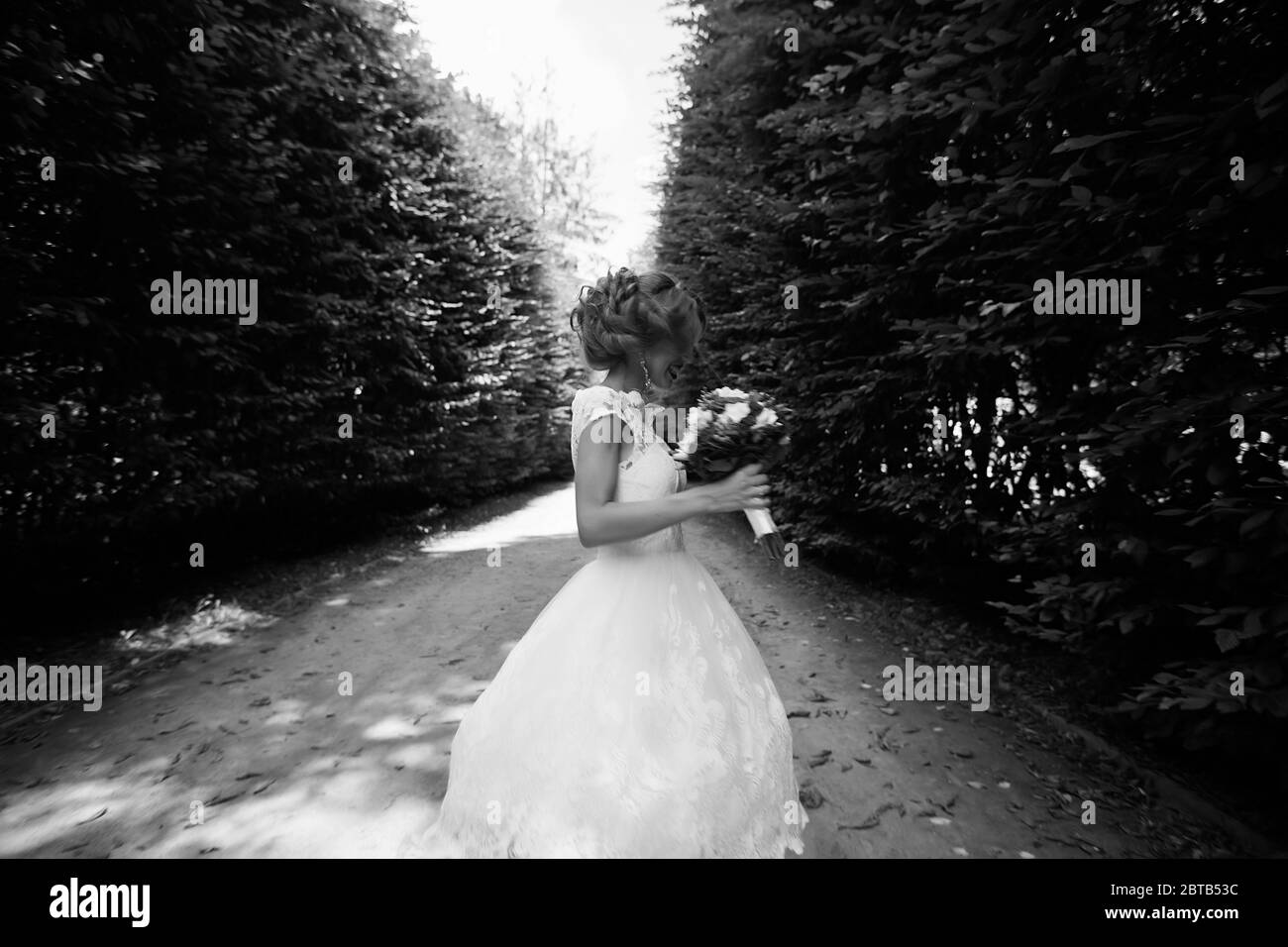 La mariée dans une robe de mariage blanche tient un bouquet sur un fond de parc vert Banque D'Images