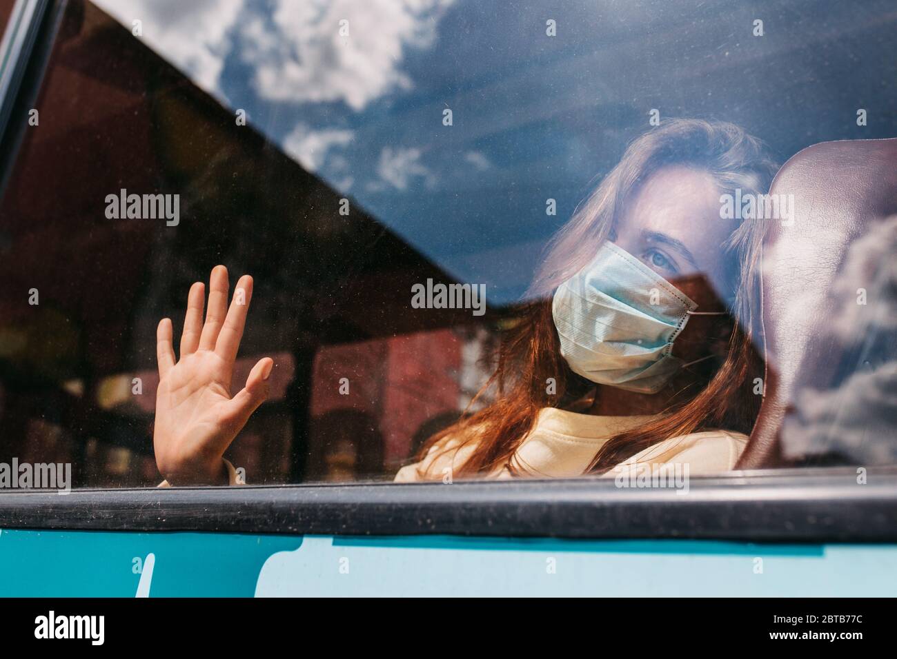 jeune femme caucasienne portant un masque facial de protection fait main regardant à l'extérieur de la fenêtre avec tristesse dans les yeux Banque D'Images