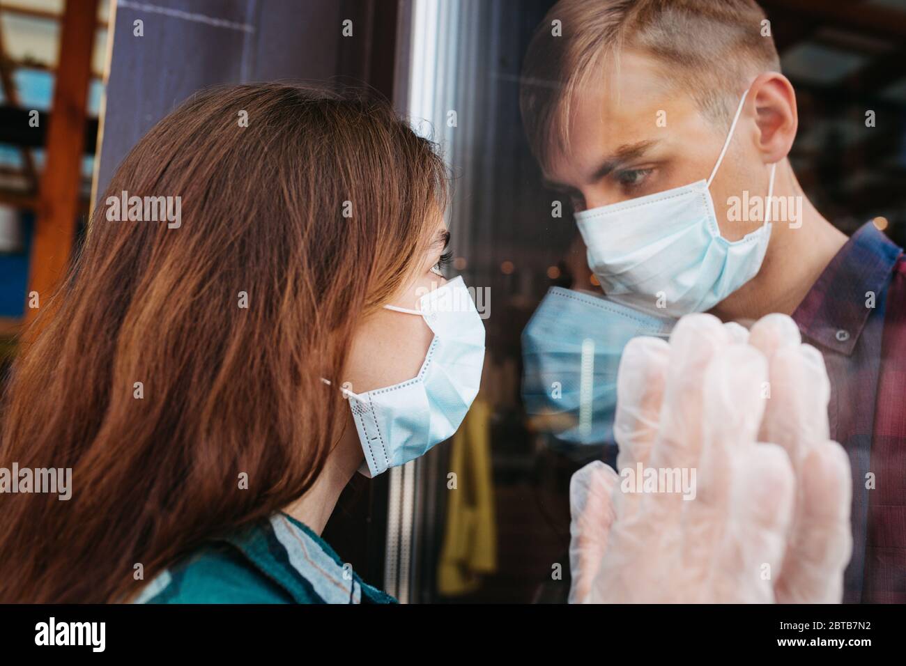 Un jeune couple, un homme et une femme dans des masques médicaux et des gants regardent chacun à travers le verre. Auto-isolation Banque D'Images